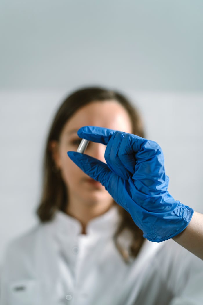 Female scientist in lab coat and gloves examining a capsule in laboratory setting.
